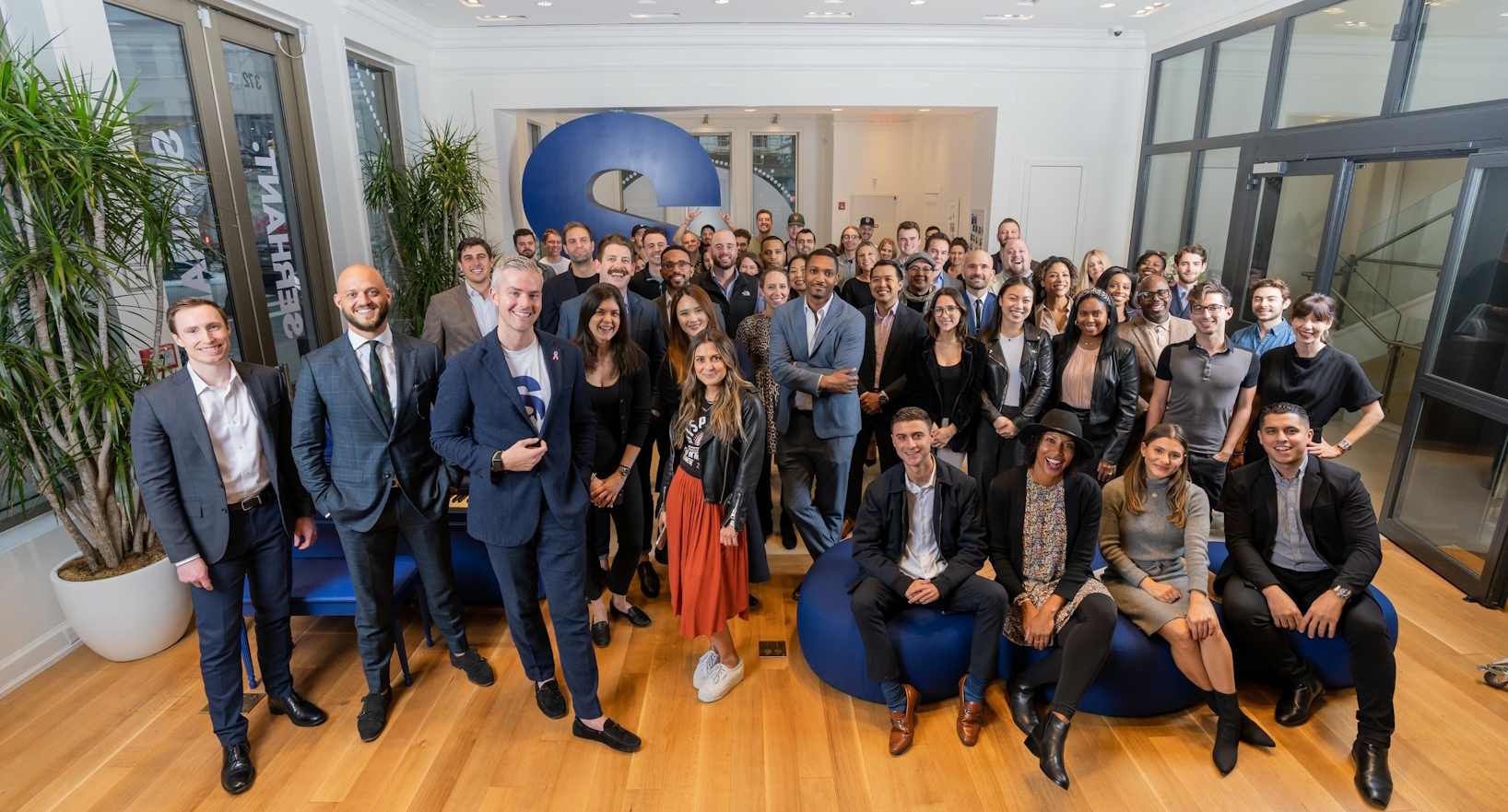 Group of diverse people led by Ryan Serhant standing in an office